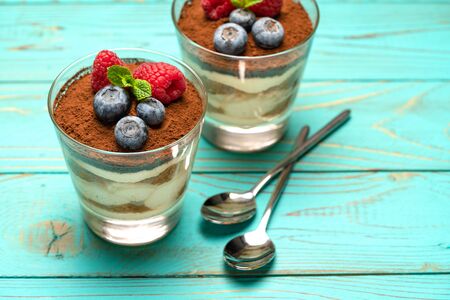 Classic tiramisu dessert with blueberries and strawberries in a glass cup on wooden backgroundの写真素材