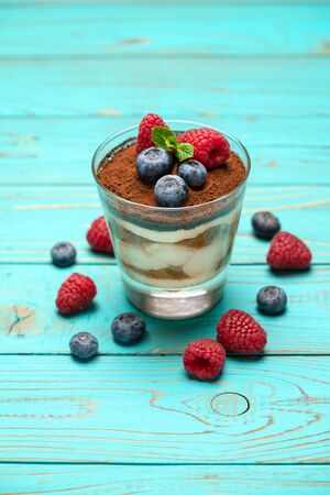 Classic tiramisu dessert with blueberries and strawberries in a glass cup on wooden backgroundの写真素材