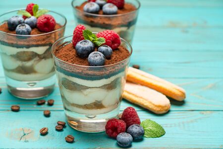 Classic tiramisu dessert with blueberries and strawberries in a glass cup and savoiardi cookies on wooden backgroundの写真素材