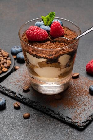 Classic tiramisu dessert portion with blueberries and raspberries in a glass cup on stone serving board on concrete backgroundの写真素材