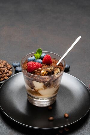Classic tiramisu dessert portion with blueberries and raspberries in a glass cup on stone serving board on concrete backgroundの写真素材