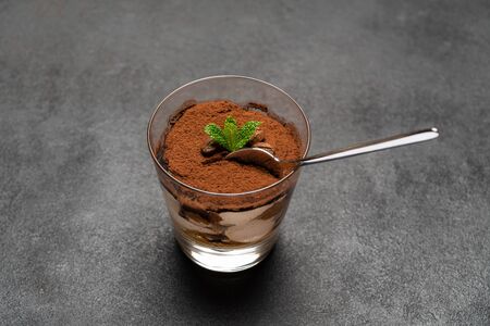 Portion of Classic tiramisu dessert in a glass cup on dark concrete background
