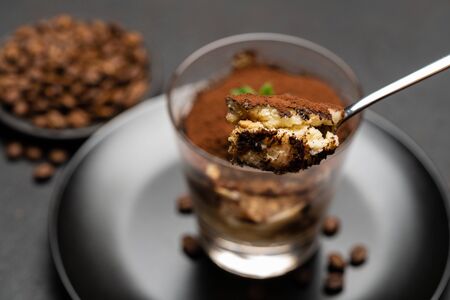 Portion of Classic tiramisu dessert in a glass cup on dark concrete background