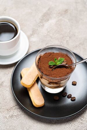 Portion of Classic tiramisu dessert in a glass cup, savoiardi cookies and espresso coffee on concrete backgroundの写真素材
