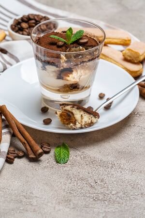 Portion of Classic tiramisu dessert in a glass, savoiardi cookies and cup of coffee on concrete backgroundの写真素材