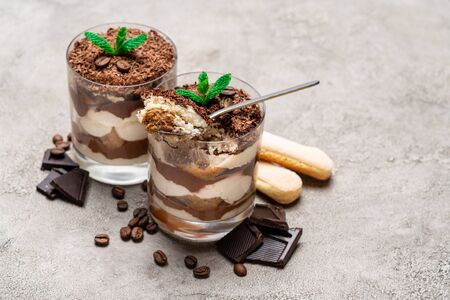 Classic tiramisu dessert in a glass cup, savoiardi cookies and pieces of chocolate on concrete background or tableの写真素材