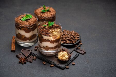 Classic tiramisu dessert in a glass cup and pieces of chocolate on stone cutting board on dark concrete background or tableの写真素材