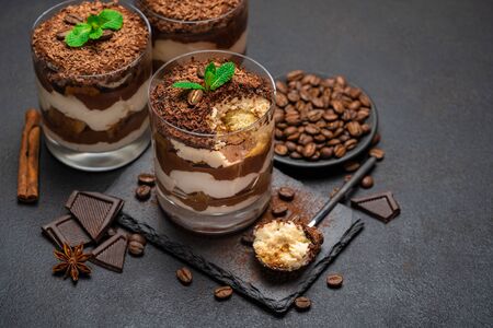 Classic tiramisu dessert in a glass cup and pieces of chocolate on stone cutting board on dark concrete background or tableの写真素材