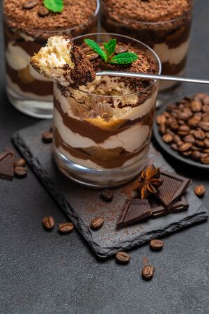 Classic tiramisu dessert in a glass cup and pieces of chocolate on stone cutting board on dark concrete backgroundの写真素材