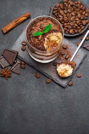 Classic tiramisu dessert in a glass cup and pieces of chocolate on stone cutting board on dark concrete backgroundの写真素材