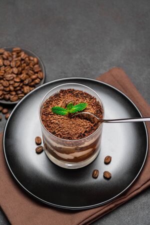 Classic tiramisu dessert in a glass cup and pieces of chocolate on dark concrete backgroundの写真素材