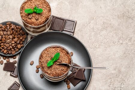 Classic tiramisu dessert in a glass cup and pieces of chocolate on concrete backgroundの写真素材
