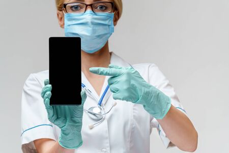 medical doctor nurse woman wearing protective mask and gloves - using mobile phoneの写真素材