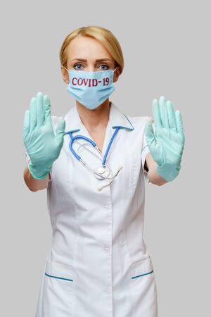 female doctor with stethoscope wearing protective mask and latex gloves over light grey backgroundの写真素材