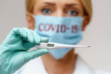 medical doctor nurse woman wearing protective mask and rubber or latex gloves - holding thermometerの写真素材