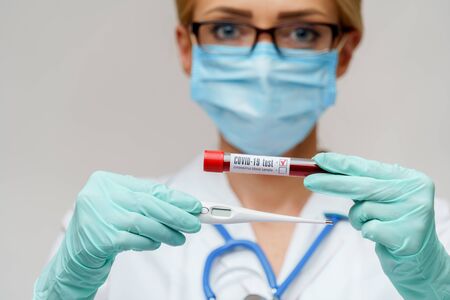 medical doctor nurse woman wearing protective mask and gloves - holding electronic thermometerの写真素材