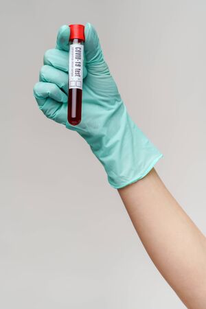 hand in latex glove holding blood in test tube close up