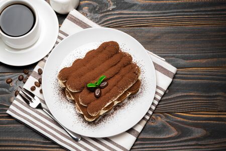 Classic tiramisu dessert on ceramic plate, milk or cream and cup of coffee on wooden backgroundの写真素材