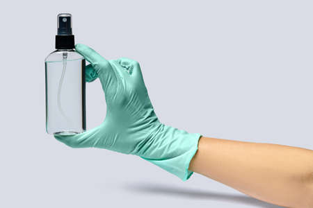 Female hand in latex rubber glove and hand sanitizer spray dispenser over light grey background.