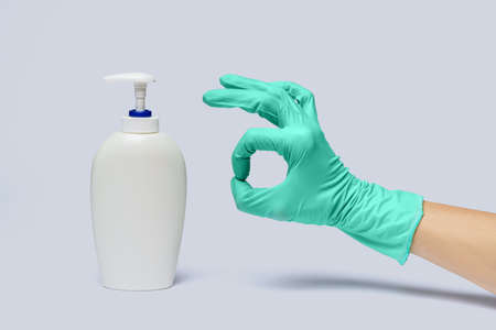 Female hand in latex rubber glove and hand sanitizer or liquid soap dispenser over light grey background.の写真素材