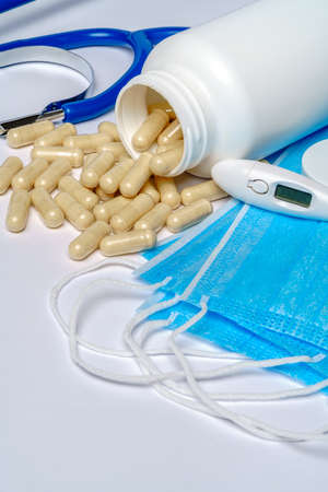 Disposable Medical protective mask with can of pills and thermometer over light grey background.