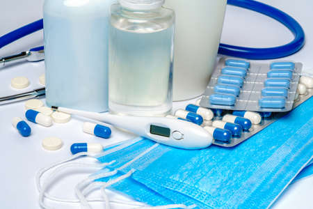 bottle of sanitizer or liquid soap, protective mask, medicine pills blisters and thermometer over light grey background.の写真素材