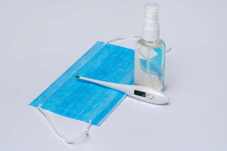 bottle of lotion, sanitizer or liquid soap, electronic thermometer and protective mask over light...