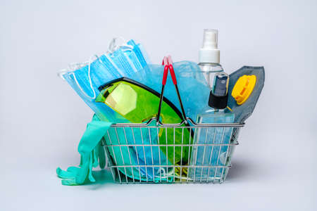 shobbing basket cart full of medical facilities - disposable medical face masks, pair of latex gloves. hat, protective glasses and bottle of sanitizer over light grey background.の写真素材