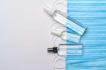 bottle of lotion, sanitizer or liquid soap and protective mask over light grey background