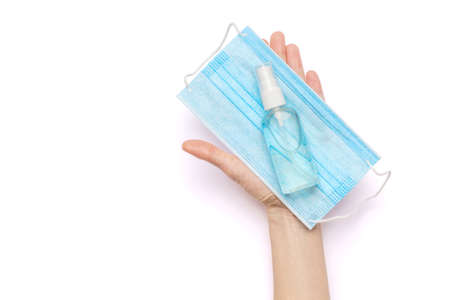 Female hands holding liquid soap or hand sanitizer spray dispenser and medical protective mask isolated on white backgroundの写真素材