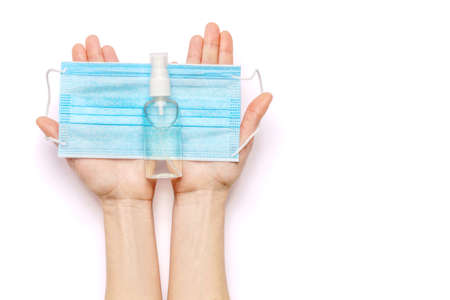 Female hands holding liquid soap or hand sanitizer spray dispenser and medical protective mask isolated on white backgroundの写真素材