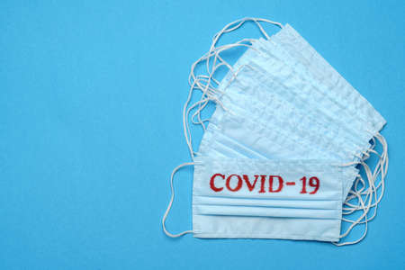 Stack of Disposable blue medical face masks with COVID-19 sign on blue backgroundの写真素材