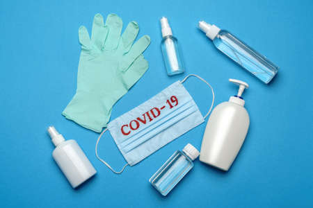 Disposable blue medical face mask with COVID-19 sign, protective goggles, rubber latex glove and hat on blue backgroundの写真素材