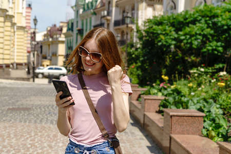 Beautiful Young Woman tourist in the City Center holding phone and making yes win gesture
