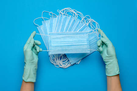 Human hand in protective glove holding face protective masks isolated on blue background