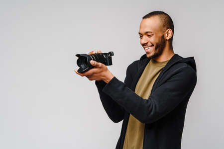 Handsome african american guy holding digital camera over light gray backgroundの写真素材
