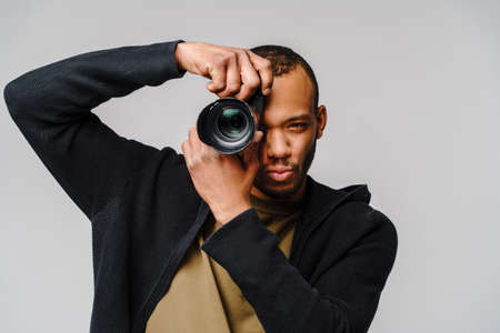 Handsome african american guy holding digital camera over light gray backgroundの写真素材
