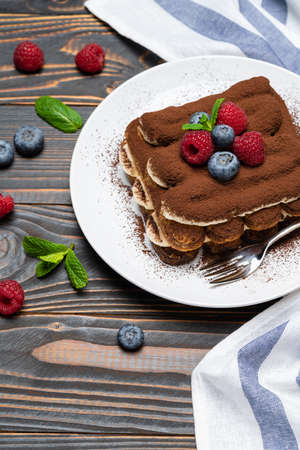 portion of Classic tiramisu dessert with raspberries and blueberries on wooden backgroundの写真素材