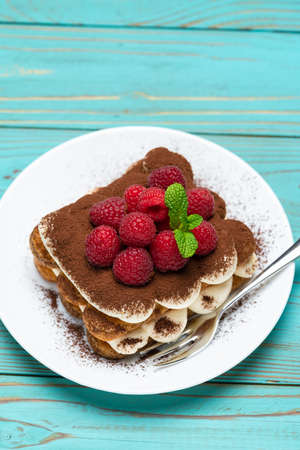portion of Classic tiramisu dessert with raspberries on blue wooden background