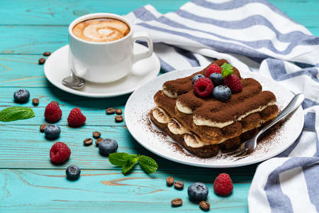 portion of Classic tiramisu dessert with raspberries and blueberries and cup of espresso coffee on...