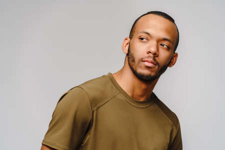 Joyful friendly african-american young man in green t-shirt over light grey background with copy spaceの写真素材