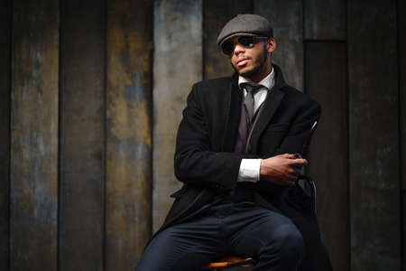 Studio shot of stylish african american man wearing coat, cap, glasses and holding smoking pipeの写真素材
