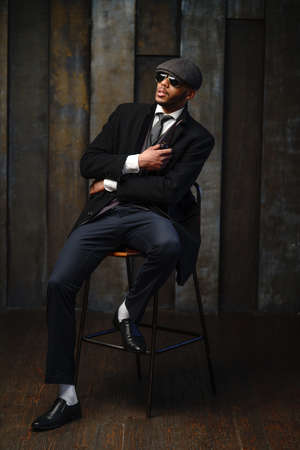 Studio shot of stylish african american man wearing coat, cap, glasses and holding smoking pipeの写真素材