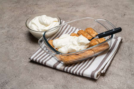 tiramisu dessert cooking - Traditional Italian Savoiardi ladyfingers Biscuits and cream in glass baking dish on concrete backgroundの写真素材