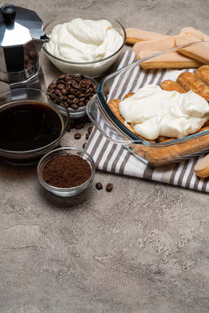 tiramisu dessert cooking - Traditional Italian Savoiardi ladyfingers Biscuits and cream in glass baking dish, coffe maker on concrete backgroundの写真素材