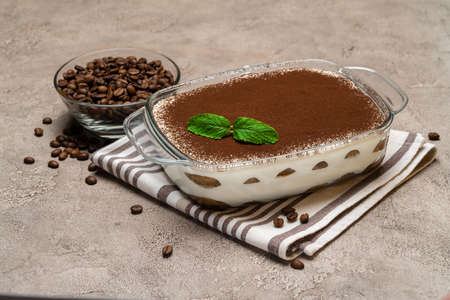 Traditional Italian Tiramisu dessert in glass baking dish on concrete background