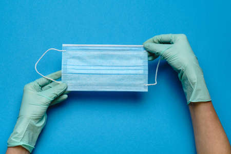 Human hand in protective gloves holding face protective mask isolated on blue backgroundの写真素材
