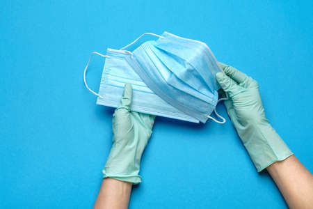 Human hand in protective gloves holding face protective mask isolated on blue background