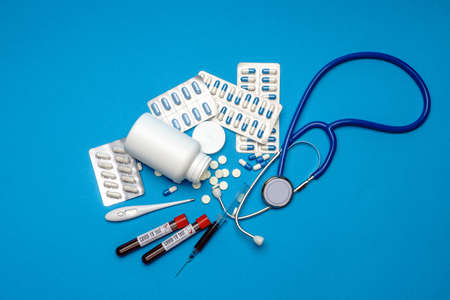 Stethoscope, syringe, thermometer, blood test tube and can of pills on blue background top view with...