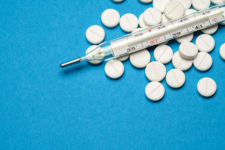 group of white pills or tablets and mercury thermometer on blue background